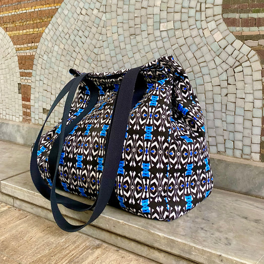 <img src="grand_cabas-molos-vue_-de-biais-pose-sur-banc-en-pierre-la-rue-avec-en-arriere-plan-mosaique-l-oeuf-centre-d-etude_jpeg" alt="