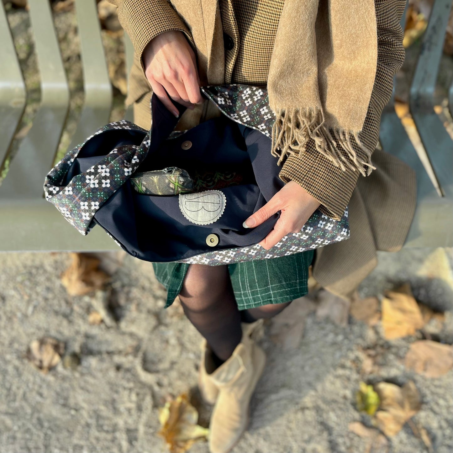 <img src=sac-hobo-hoguette-tenu-dans-les-bras-et_ouvert-avec-vue-sur-le-logo-et-le-fermoir-sol-tapisse-de-feuilles-mortes.jpeg" alt="